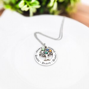K&ouml;nnte beinhalten: Eine silberfarbene Halskette mit einem Baum-Anh&auml;nger. Der Anh&auml;nger hat ein Baumdesign mit bunten Edelsteinen und den Namen "Drake", "Grace", "Grant" und "Lucas" am Rand eingraviert. Die Halskette liegt auf einer wei&szlig;en Oberfl&auml;che.