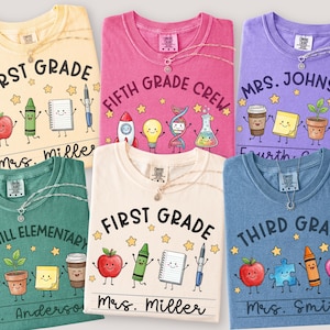 May include: Six short-sleeve t-shirts in yellow, pink, purple, green, cream, and blue. Each shirt features school-themed graphics like apples, crayons, notebooks, and science icons, with printed text including grade levels and teacher names.