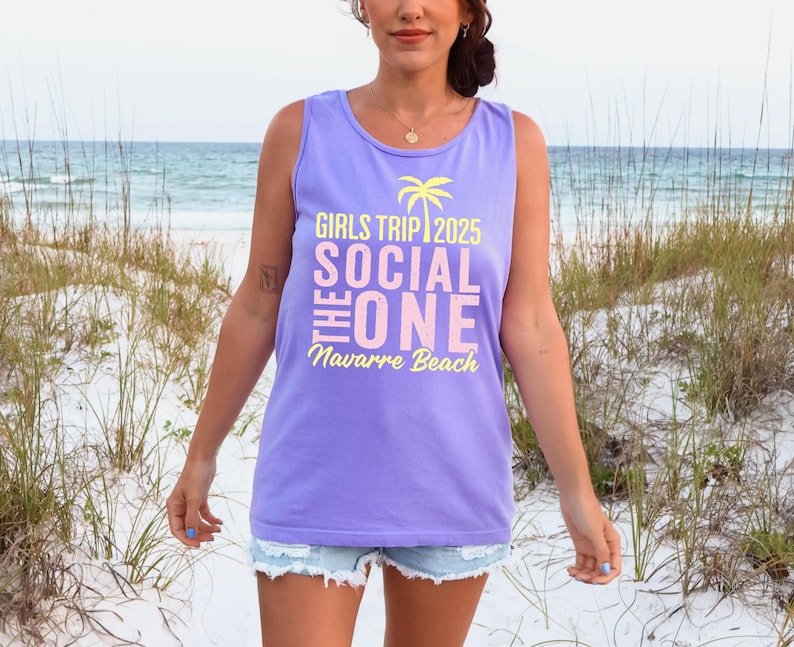 May include: A light purple sleeveless tank top featuring a yellow palm tree icon and text that reads GIRLS TRIP 2025, THE SOCIAL ONE, and Navarre Beach in a mix of yellow and light pink lettering printed on the front of the garment.
