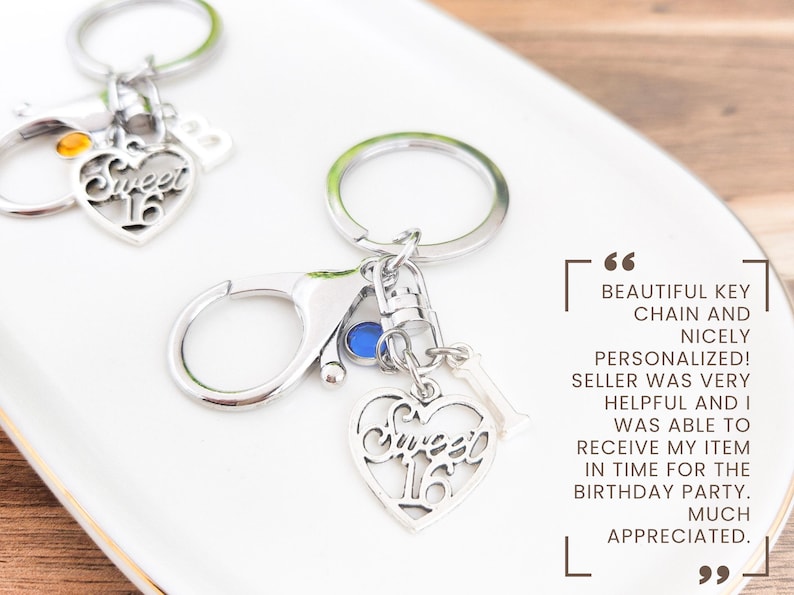 May include: Silver keychains with a heart-shaped charm that says "Sweet 16". The keychains have a clasp and a small charm with the number "1". The background is a white plate.