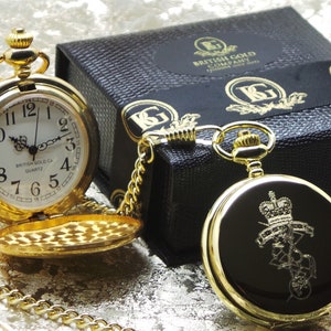 May include: A gold pocket watch with a black face and a chain. The watch is in a black box with the words "British Gold Company" printed on it.