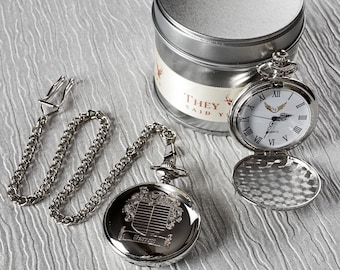 Puede incluir: Un reloj de bolsillo plateado con una esfera blanca y marcadores de hora romanos negros. El reloj está abierto y la parte posterior es visible. El reloj está en una cadena plateada con un cierre. El reloj está en una lata plateada con las palabras "They Said Y" en la etiqueta.