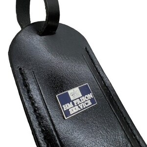 May include: Black leather luggage tag with a silver metal emblem that reads "HM PRISON SERVICE" in blue lettering.