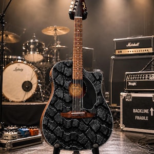 K&ouml;nnte beinhalten: Eine akustisch-elektrische Gitarre mit einem einzigartigen schwarzen Reifenprofil-Design auf dem Korpus, ausgestellt auf einem schwarzen St&auml;nder. Die Gitarre hat einen braunen Hals und Kopfplatte, mit dem Fender-Logo. B&uuml;hnenbeleuchtung beleuchtet das Instrument.