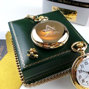 May include: Gold pocket watch with a Masonic symbol engraved on the front. The watch comes in a green velvet box with a gold chain.