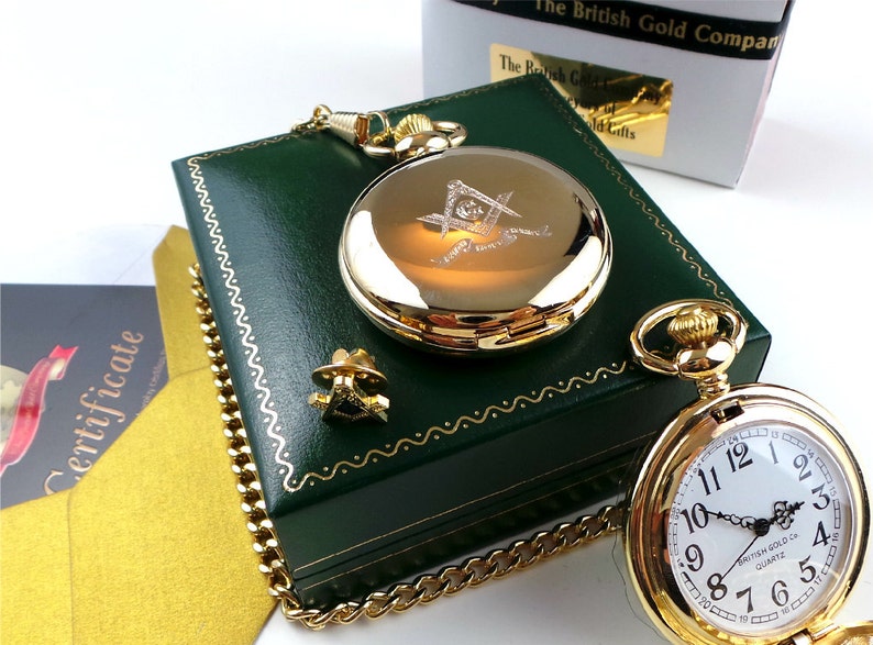 May include: Gold pocket watch with a Masonic symbol engraved on the front. The watch comes in a green velvet box with a gold chain.