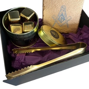 May include: A black gift box with a gold metal container of gold ice cubes, a gold metal coaster with a Masonic symbol, and gold metal tongs.