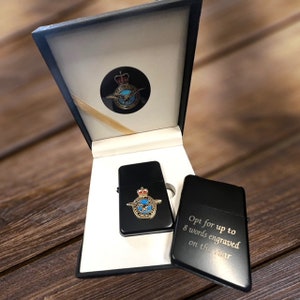 Può includere: Un accendino nero con un emblema dorato di un'aquila coronata con le ali spiegate. L'accendino è in una scatola nera con una scritta dorata che dice "Opt for up to 8 words engraved on the rear".