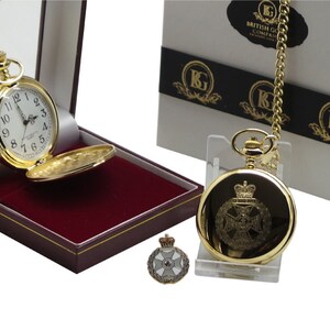 May include: Gold pocket watch with a white face and black Roman numeral hour markers. The watch is in a red velvet box with a gold chain and a matching lapel pin. The box has the text "British Gifts Company" on it.