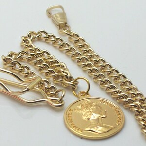 May include: A gold pocket watch chain with a round pendant featuring a profile of Queen Elizabeth II. The chain has a lobster clasp and a swivel hook.