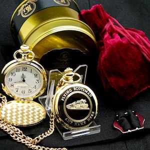 May include: Gold pocket watch with a chain, a velvet pouch, and a tin box. The watch face has Roman numerals and the words "British Gold Company" on the dial. The back of the watch has an engraved image of a train with the words "Flying Scotsman" and "Any Name Here".