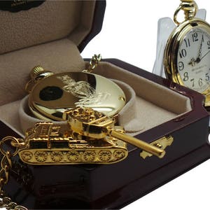 May include: A gold pocket watch with a chain and a gold tank charm in a wooden box. The watch face has Roman numerals and the words "Westminster England" printed on it.