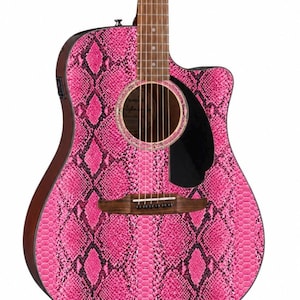 May include: Acoustic guitar with a vibrant pink snakeskin pattern. The guitar features a dark brown neck and body edges, a black pickguard, and a sound hole with a decorative ring. The strings and bridge are visible, showcasing the instrument's design.