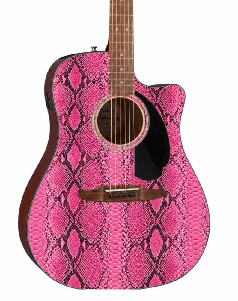 May include: Acoustic guitar with a vibrant pink snakeskin pattern. The guitar features a dark brown neck and body edges, a black pickguard, and a sound hole with a decorative ring. The strings and bridge are visible, showcasing the instrument's design.
