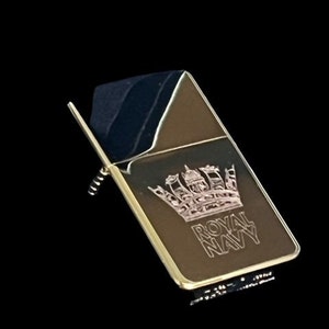 Op de afbeelding: Gouden aansteker met een zwarte bovenkant en een roze gegraveerde kroon en de woorden "Royal Navy".