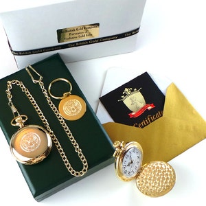 May include: A gold pocket watch with a chain and a small gold charm. The watch is in a green velvet box. The watch has a white face with black numbers and hands. The watch is open and the back is engraved with a design. The watch comes with a certificate of authenticity.