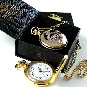 May include: A gold pocket watch with a white face and black Roman numeral markings. The watch is in a black box with a gold chain.
