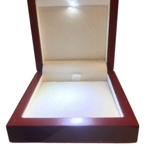 Może przedstawiać: Drewniana skrzynka w kolorze czerwonym z białym aksamitnym wnętrzem i wbudowanym oświetleniem LED. Skrzynka jest otwarta, a światło jest włączone.