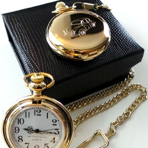 May include: A gold pocket watch with a white face and black hands. The watch has a gold chain and is in a black box. The watch face has the text "BRITISH GOLD Co. QUARTZ".