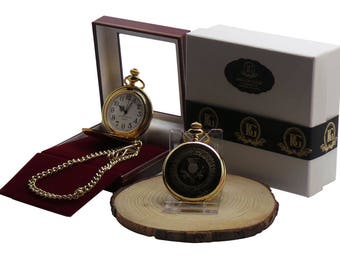Puede incluir: Un reloj de bolsillo dorado con una cadena y un diseño de cardo en la esfera, en una caja de presentación con una cinta negra y dorada.
