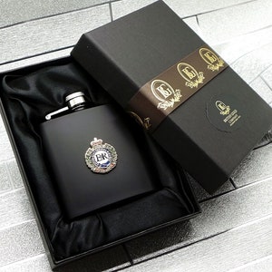 Könnte beinhalten: Schwarze Flasche mit silbernem Deckel und einem goldenen Wappen mit den Buchstaben "E.R." in einem Kranz. Die Flasche befindet sich in einer schwarzen, samtig ausgekleideten Box mit einem braunen Band und dem Text "British Gold Company" auf einem weißen Kreis.