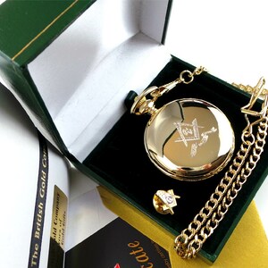 May include: A gold pocket watch with a chain and a small gold pin in a green velvet box. The watch face has an engraved design.