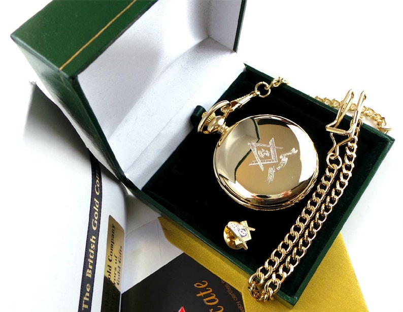May include: A gold pocket watch with a chain and a small gold pin in a green velvet box. The watch face has an engraved design.