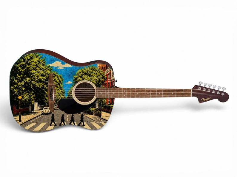 Puede incluir: Guitarra ac&uacute;stica con un dise&ntilde;o personalizado que presenta la ic&oacute;nica escena de Abbey Road. La guitarra tiene un cuerpo marr&oacute;n, una boca negra y un clavijero Fender. La imagen muestra un d&iacute;a soleado con &aacute;rboles y edificios.
