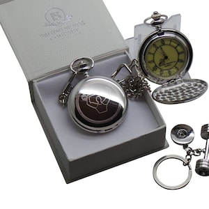 May include: A silver pocket watch with a white face and black hands, a silver chain, and a silver dumbbell keychain. The watch is in a white box with the text "British Silver Company" on the lid.