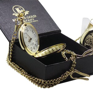May include: A gold pocket watch with a white face and black Roman numeral hour markers. The watch is in a black box with a gold chain. The box has the text "British Gold Company" on it.