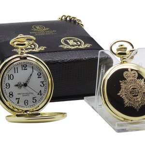Op de afbeelding: Een gouden zakhorloge met een witte wijzerplaat en zwarte Romeinse cijfers. Het horloge heeft een gouden ketting en zit in een zwarte lederen doos met de woorden "British Gold Company" erop gegraveerd. De achterkant van het horloge heeft een gouden embleem met een kroon en de letters "E.R."