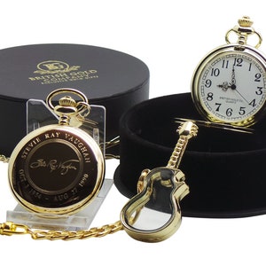 Könnte beinhalten: Goldene Taschenuhr mit Kette, einer Gitarrenform-Box und einer schwarzen Box mit der Aufschrift "BRITISH GOLD COMPANY" und "Exclusive Gold Gifts". Das Zifferblatt der Uhr hat römische Ziffern und die Worte "BRITISH GOLD CO. QUARTZ". Die Uhr ist graviert mit "STEVIE RAY VAUGHAN" und seiner Unterschrift, sowie den Daten "OCT 3 1954" und "AUG 27 1990".