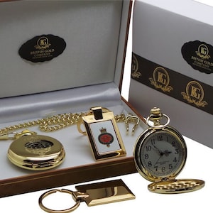 Pode incluir: Um conjunto de presente com um relógio de bolso dourado com corrente, um porta-chaves e uma etiqueta retangular. O relógio tem um mostrador branco com algarismos pretos. A caixa tem o texto "British Gold Company".
