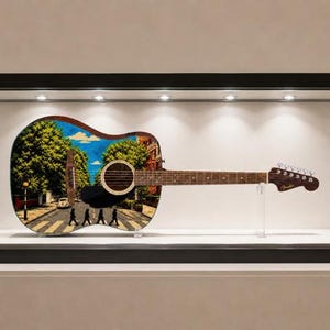 Puede incluir: Guitarra ac&uacute;stica con un dise&ntilde;o personalizado que presenta la ic&oacute;nica escena del cruce de Abbey Road. La guitarra se exhibe en una vitrina de cristal, mostrando la colorida obra de arte en el cuerpo. La guitarra tiene un m&aacute;stil y clavijero marrones.