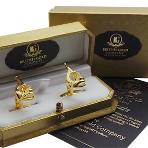 Op de afbeelding: Gouden manchetknopen in een presentatiedoos met de tekst "The British Gold Company" op de deksel. De manchetknopen zijn bloemvormig met een gouden afwerking.