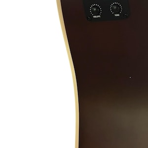 Puede incluir: Primer plano del cuerpo de una guitarra ac&uacute;stica marr&oacute;n oscuro con un borde color crema. Se ve un panel de control negro con perillas de volumen y tono. La guitarra tiene el logotipo de Fender.
