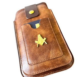 May include: A brown leather phone case with a gold Masonic symbol and a pocket for a credit card.