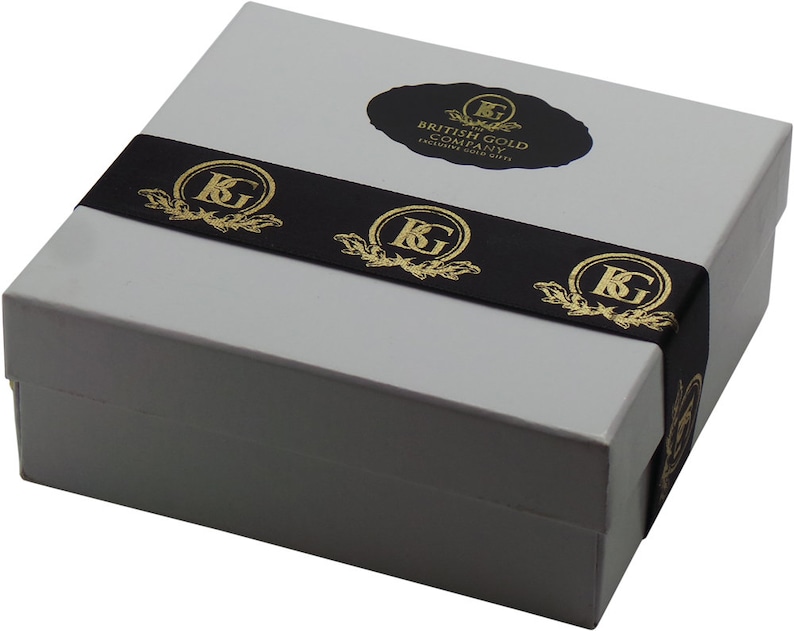 May include: A gray gift box with a black ribbon and gold lettering. The ribbon has the text "The British Gold Company, Exclusive Gold Gifts" and a gold "KG" logo repeated three times.