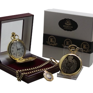 May include: A gold pocket watch with a chain and a small box. The watch face has Roman numerals and the watch case has an engraved design. The box is red and has a gold trim. The watch is in a white box with the words "British Gold Company" printed on it.