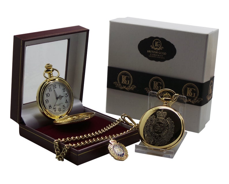 May include: A gold pocket watch with a chain and a small box. The watch face has Roman numerals and the watch case has an engraved design. The box is red and has a gold trim. The watch is in a white box with the words "British Gold Company" printed on it.