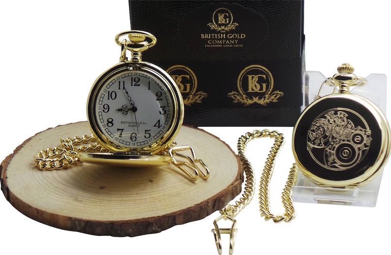 May include: A gold pocket watch with a white face and black Roman numeral hour markers. The watch has a gold chain and is in a box with the text "British Gold Company" on it.