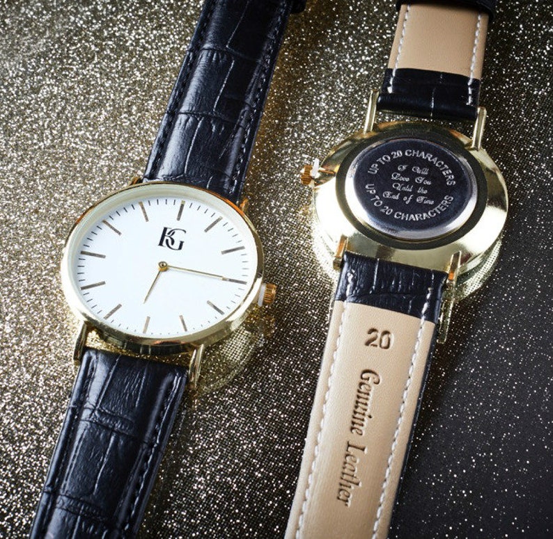 Op de afbeelding: Twee goudkleurige polshorloges met zwarte leren banden. Het horloge aan de linkerkant heeft een witte wijzerplaat met zwarte wijzers en een gouden 'KG'-logo. Het horloge aan de rechterkant heeft een gouden achterkant met een inscriptie die luidt 'Tot 20 tekens Ik zal van je houden tot het einde der tijden Tot 20 tekens'. De band van het horloge aan de rechterkant heeft '20 Echt leer' gegraveerd op de achterkant.