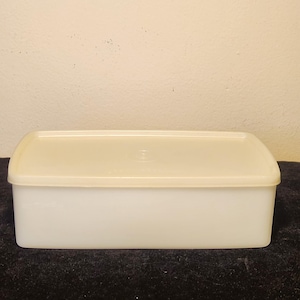May include: A rectangular, off-white plastic storage container with a matching fitted lid. The container features a smooth, opaque finish and a simple, functional design with rounded corners, providing a clean look for organizing various household items.