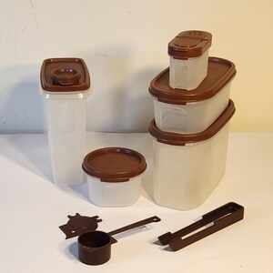 May include: A collection of brown-lidded, clear plastic food storage containers of various sizes, including rectangular and square shapes. Also included are a small scoop, a spatula, and a pair of tongs. The items are arranged on a white surface.