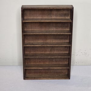 Puede incluir: Un estante de pared rectangular de madera con un acabado marrón oscuro y veta de madera visible. La unidad consta de seis compartimentos horizontales abiertos apilados verticalmente, proporcionando múltiples niveles de almacenamiento en un marco simple.