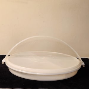 Puede incluir: Contenedor de plástico redondo de color blanquecino con un asa arqueada transparente. El contenedor tiene una tapa y una base, adecuado para el almacenamiento o transporte de alimentos. El diseño es simple y funcional.