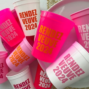 Peut inclure: Un ensemble de gobelets en plastique rose et blanc avec le texte "Rendez Vous 2024" imprim&eacute; dessus. Les gobelets sont dispos&eacute;s en pile, certains se chevauchant.
