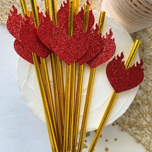 May include: A set of gold foil straws with red glitter heart-shaped toppers. The toppers have a flame design.