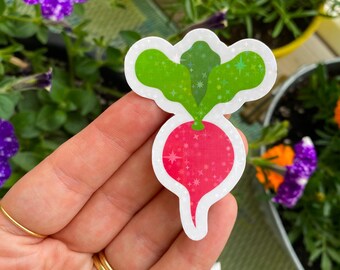 May include: A sticker featuring a radish design with a pink body and green leaves. The sticker has a white border and a sparkly finish. The background includes flowers and greenery.