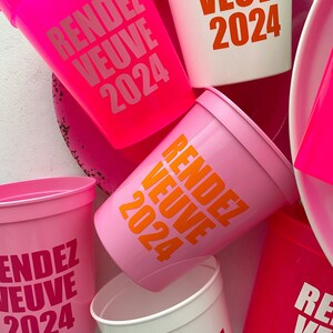 Peut inclure: Un ensemble de six gobelets en plastique rose et blanc avec le texte "Rendez Vous 2024" imprim&eacute; dessus. Les gobelets sont empil&eacute;s les uns sur les autres.
